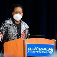 woman behind podium wearing mask speaks to audience